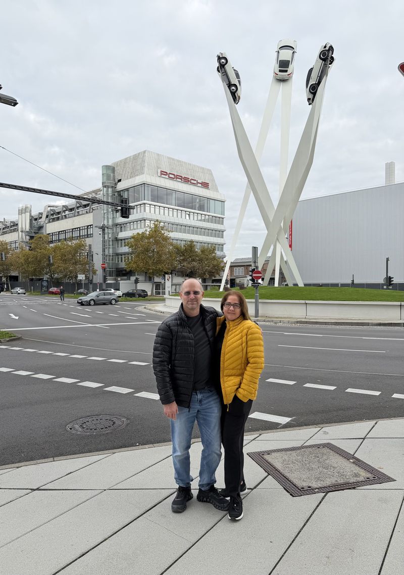 Vincente D'Ingianni and his wife in front of the Porscheplatz sculpture, three Porsche 911s on its white columns, outside the Porsche Museum
